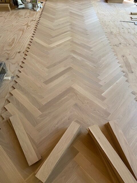 the first strip of oak herringbone parquet has been placed